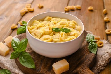 Tortellini mignon ahşap bir tahtada fesleğen ve parmesanlı. Bologna ve Emilia Romagna mutfağının spesiyaliteleri: Cappelletti, et ve sebzeli taze yumurtalı makarna..