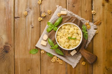 Tortellini mignon ahşap bir tahtada fesleğen ve parmesanlı. Bologna ve Emilia Romagna mutfağının spesiyaliteleri: Cappelletti, et ve sebzeli taze yumurtalı makarna..