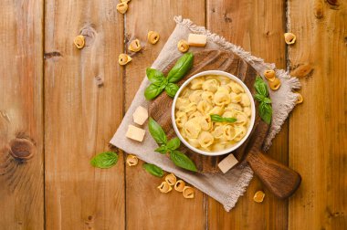 Tortellini mignon on a wooden board with basil and parmesan. Specialties of the cuisine from Bologna and Emilia Romagna: Cappelletti, fresh egg pasta with meat and vegetables filling. clipart