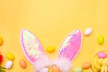 Bahar. Paskalya çikolatası yumurtaları, sarı arka planda pembe tavşan kulakları. 
