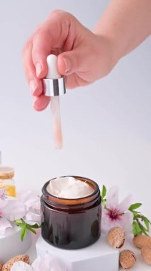 Bir kadın ellerine krem sürer. Badem yağı ve vitaminli el kremi. Vücut sağlığı ve güzellik. Parlak bir arkaplan, kozmetik ve doğal badem çiçekleriyle dolu kavanozlar..