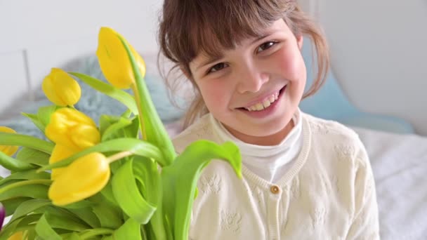 Elinde parlak lalelerden oluşan bir buket olan küçük bir kız, 8 Mart 'ta ya da Anneler Günü' nde bunları annesine veriyor. Annem ya da büyükannem için bir hediye. Bahar çiçeği buketi. Dikey — Stok video