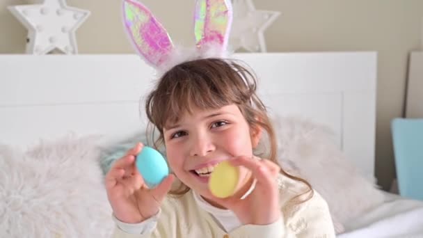 Petite fille heureuse dans les oreilles de lapin s'amuse, jouer avec des œufs de Pâques colorés. Œufs en chocolat de différentes couleurs pour Pâques entre les mains d'un enfant. — Video