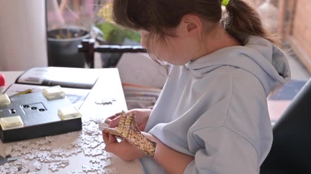Verstreute Rätsel auf dem Tisch. Kleines Mädchen mit europäischem Aussehen spielt im Zimmer Brettspiele. Nahaufnahme einer Hand mit Details und Teilen aus einem 3D-Puzzle. — Stockvideo