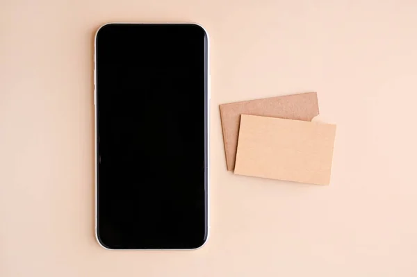Κινητό τηλέφωνο mockup με λευκή οθόνη και επαγγελματικές κάρτες που απομονώνονται σε μπεζ χαρτί. Επαγγελματική κάρτα από χαρτί χειροτεχνίας και έξυπνο τηλέφωνο. — Φωτογραφία Αρχείου