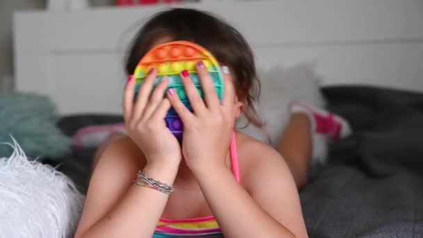 Little girl plays with pop it sensory toy. The baby clicks on colorful rainbow soft soft silicone bubbles. — Stock Video