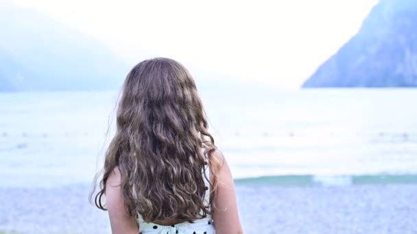 Niña feliz exuda emociones de alegría, ella está girando jugando y sonriendo. Un niño en la orilla de un lago de montaña pasa tiempo con su familia en el verano. Concepto de Felices Fiestas con Padres. — Vídeos de Stock