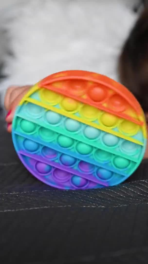 Kleines Mädchen spielt mit Pop it sensorischem Spielzeug. Das Baby klickt auf bunte regenbogenweiche Silikonblasen. — Stockvideo