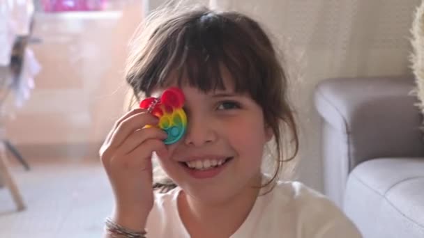 Little girl plays with pop it sensory toy. The baby clicks on colorful rainbow soft soft silicone bubbles. — Stock Video