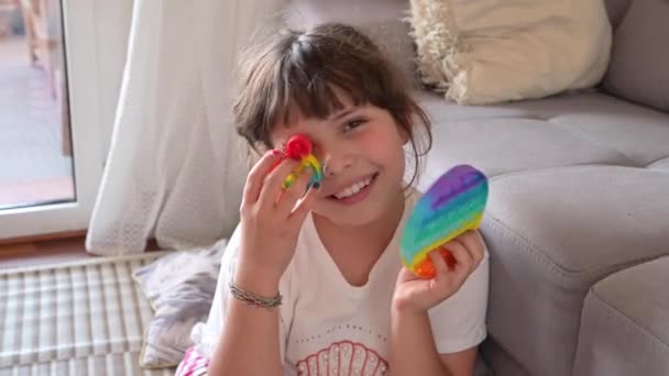 Meisje speelt met pop it sensorisch speelgoed. De baby klikt op kleurrijke regenboog zachte siliconen bellen. — Stockvideo