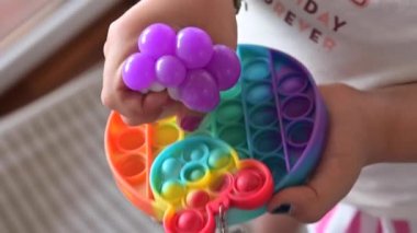 Küçük kız, pop it duyusal oyuncağıyla oynuyor. Bebek renkli gökkuşağına tıklıyor yumuşak yumuşak silikon kabarcıklar.