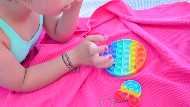 Petite fille joue avec pop it jouet sensoriel. Le bébé clique sur des bulles de silicone doux et doux arc-en-ciel coloré. — Video