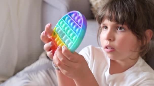 Little girl plays with pop it sensory toy. The baby clicks on colorful rainbow soft soft silicone bubbles. — Stock Video