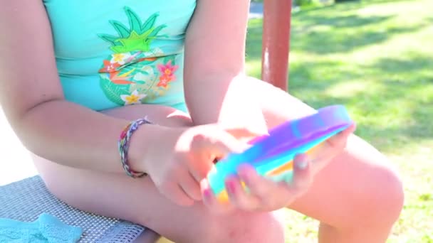 Kleines Mädchen spielt mit Pop it sensorischem Spielzeug. Das Baby klickt auf bunte regenbogenweiche Silikonblasen. — Stockvideo