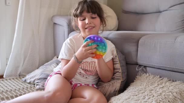 Little girl plays with pop it sensory toy. The baby clicks on colorful rainbow soft soft silicone bubbles. — Stock Video