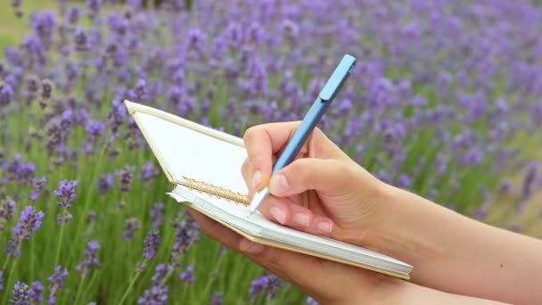 Ung kvinna gör anteckningar i en personlig dagbok bland lavendel blommor. — Stockvideo