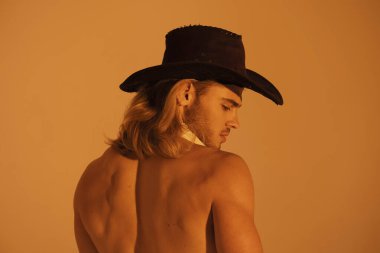 Seksi spor kaslı kaslı sarışın, uzun saçlı, inek yayı şapkalı, turuncu izole yazı tipi arka planlı.