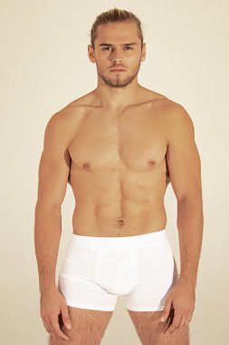 Seksi spor kaslı, kaslı, sarışın, uzun saçlı, beyaz iç çamaşırlı, beyaz tenli yazı tipi arka planlı.