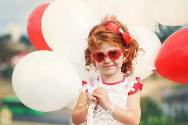 Piccola ragazza riccia che tiene palloncini rossi e bianchi fuori — Foto Stock