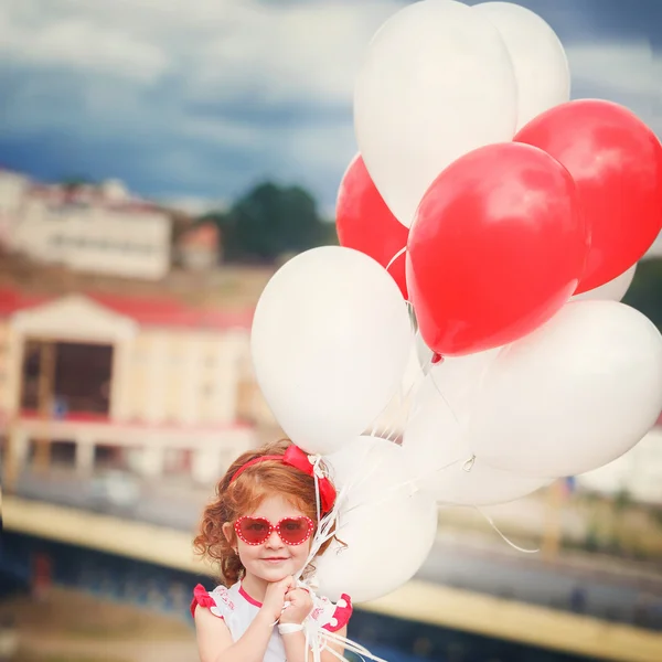Piccola bella ragazza riccia con palloncini rossi e bianchi nel p — Foto Stock