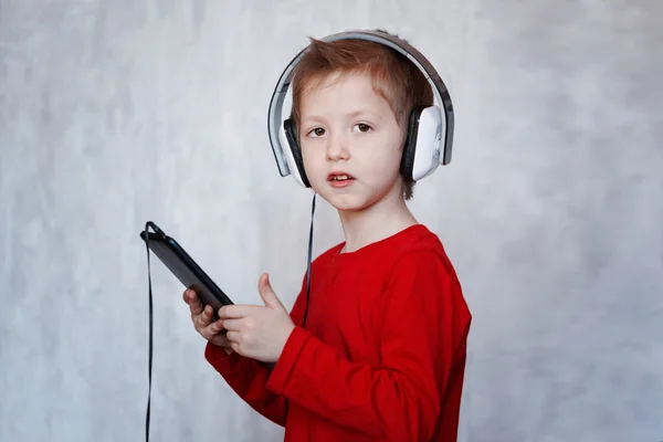 Niño pequeño con auriculares usando el panel táctil, escuchando música con —  Fotos de Stock