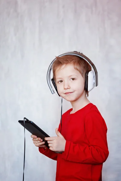 Lindo niño escuchando música con auriculares y tabletas, i —  Fotos de Stock