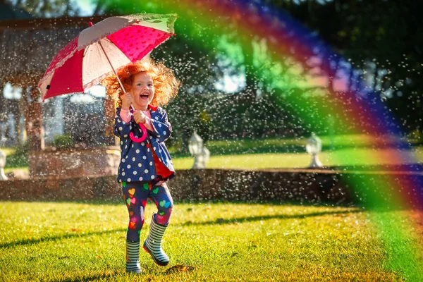 Laughing girl in the rain under umbrela with a rainbow. Happy and healthy childhood concept — Stock Photo, Image