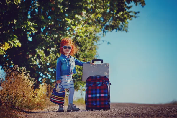 Krullend meisje met grote koffer permanent op weg en wachten op een bus of auto. — Stockfoto