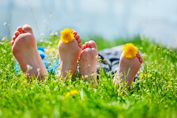 De voeten van de kinderen met paardebloem bloemen in zonnige dag op groene gras liggen. Concept happy chidlhood. — Stockfoto