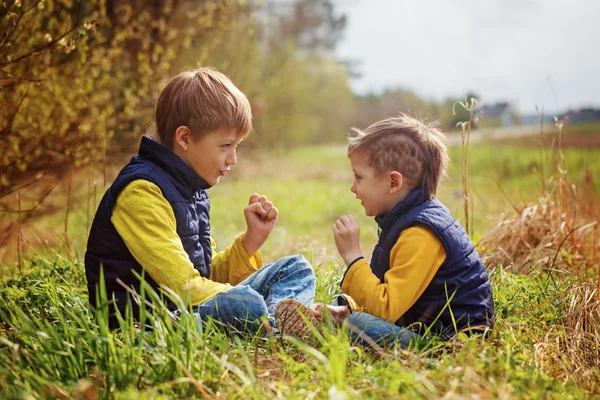 Two little brothers play in rock-paper-scissors sitting on grass — Stock Photo, Image