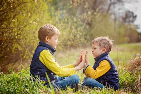 Taş-kağıt-makas çimenlerin üzerinde oturan iki küçük kardeş oynamak — Stok fotoğraf
