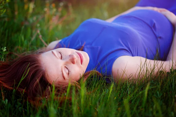 Zwanger meisje is in een gras leggen en dromen over haar pregna — Stockfoto