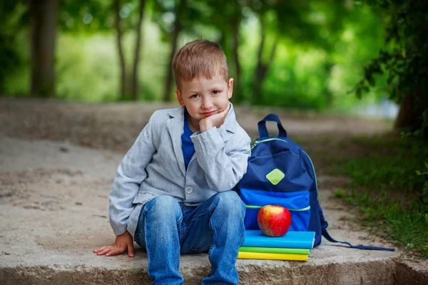 Zabawny mały chłopiec siedzi na kamieniu z książek, jabłko i backpac — Zdjęcie stockowe