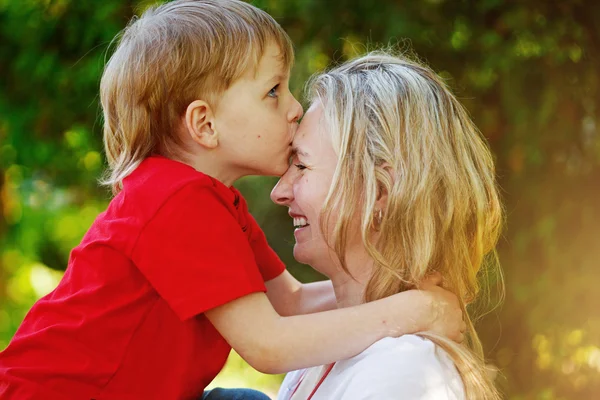 Menino feliz abraçando e beijando sua mãe sobre backg verde — Fotografia de Stock