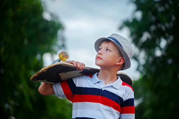 Roztomilý chlapec s skateboard v ruce venku. Nosit čepici a st — Stock fotografie