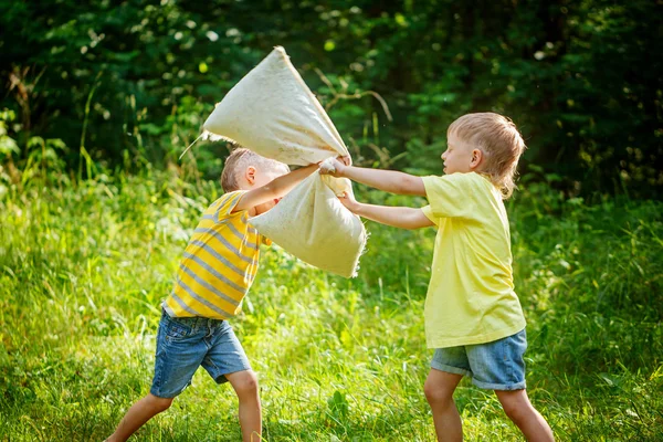 Bambini che combattono insieme a cuscini in un soleggiato giardino estivo — Foto Stock