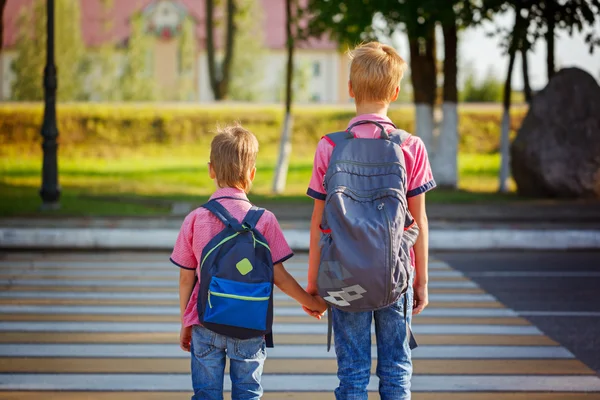 Two kids with backpacks walking on the road, holding. School tim — Stock Photo, Image