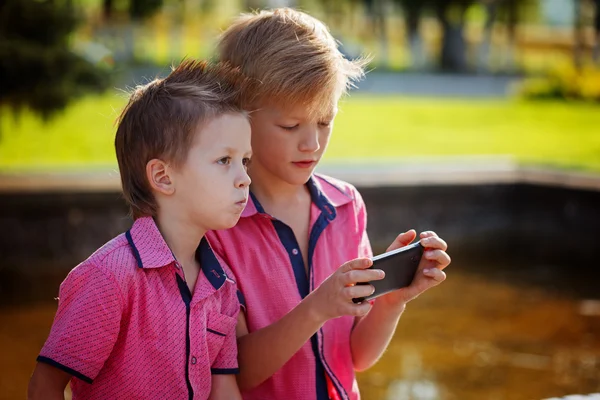 Zwei kleine Jungen spielen bei sonnigem Wetter mit dem Handy. — Stockfoto