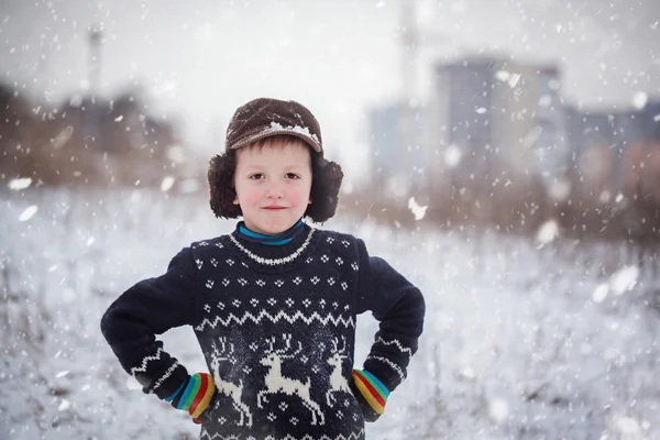 Winter portrait of little kid boy wearing a knitted sweater with deers, outdoors during snowfall. — Stock Photo, Image