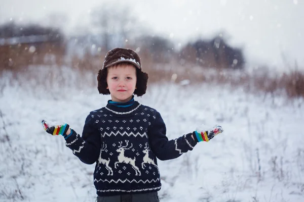 Winter portrait of little kid boy wearing a knitted sweater with deers, outdoors during snowfall. — Stock Photo, Image