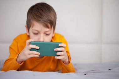 Akıllı telefonuyla bilgisayar oyununda oynayan sevimli bir çocuk. Çocuk video oyunu oynarken eğleniyor. Sosyal ve teknoloji kavramı