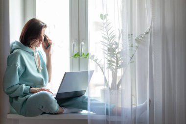 Pencere kenarında oturan genç bir kadın, elinde defterle cep telefonuyla konuşuyor. Evde çalışan, dizüstü bilgisayarda çalışan bir kız. Bağımsızlığı kabul et