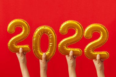 Kırmızı arka planda 2022 'nin altın rakamlarını tutan çocuk elleri. Mutlu yıllar 2022 Kutlama Konsepti.