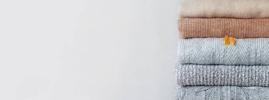 Tarafsız bir arka planda bir yığın samimi sonbahar ve kış süveteri. Sıcaklık ve rahat kıyafetler kavramı. Pankart