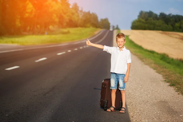 Усміхнена дитина з валізою подорожує автостопом. літня дорога — стокове фото