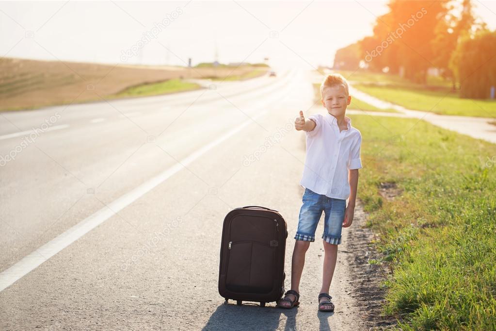 Smiling child with suitcase traveling hitchhiking. summer road  