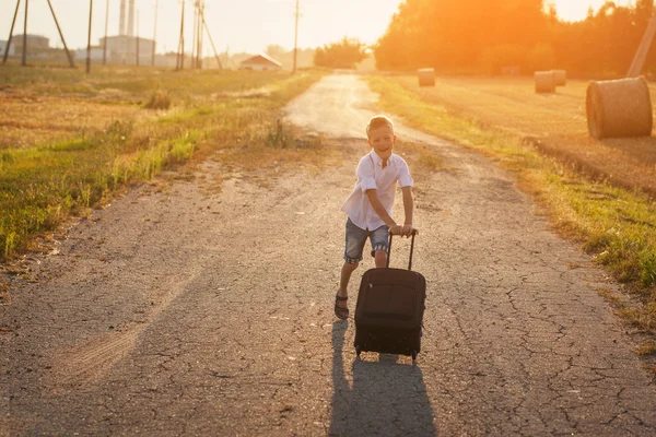 Il ragazzo felice corre con una valigia in una giornata di sole estiva — Foto Stock