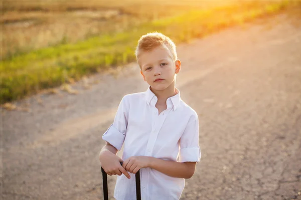 Portrét chlapce drží rukojeť kufru ve slunné da — Stock fotografie