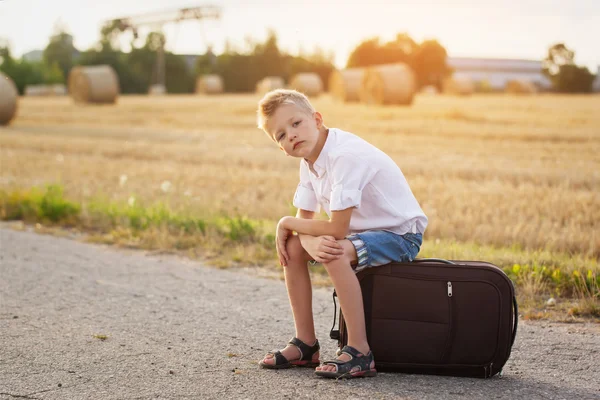 Barnet sidder på en kuffert om sommeren solskinsdag, rejser - Stock-foto