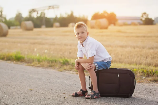 Il bambino felice si siede su una valigia nella giornata di sole estiva, il — Foto Stock